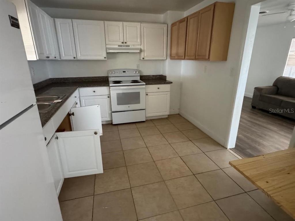 A kitchen features white and wood-toned cabinets, a white stove, and light-colored floor tiles — 1412 N GARFIELD AVENUE, DELAND, FL