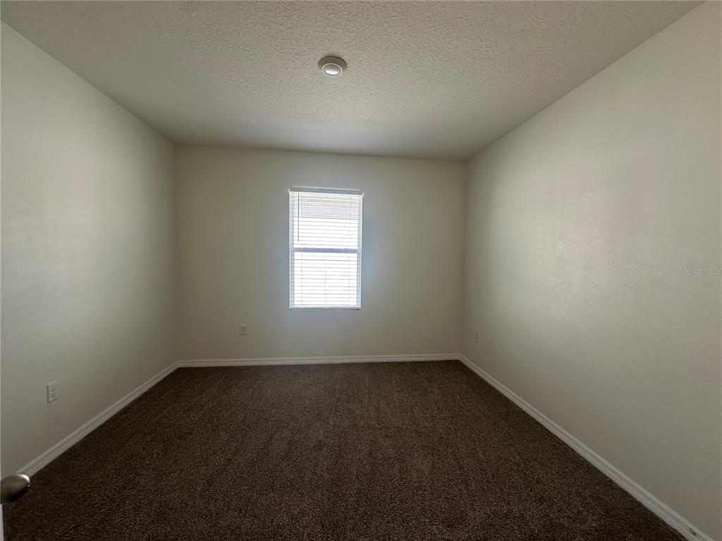 An empty bedroom features beige walls, brown carpeting, and a single window with blinds — 1292 SUGARWOOD STREET, DAVENPORT, FL