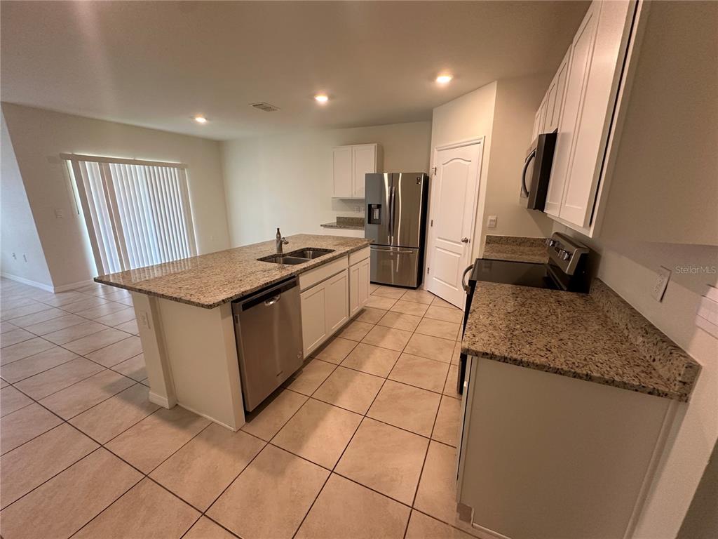 A kitchen features white cabinets, granite countertops, stainless steel appliances, and tile flooring — 1292 SUGARWOOD STREET, DAVENPORT, FL