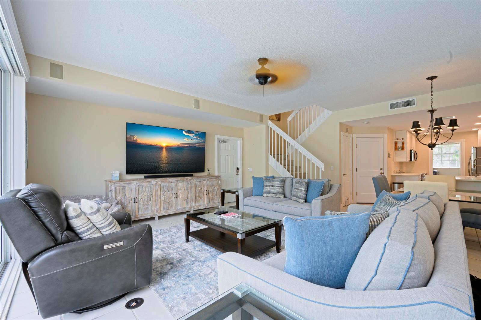 A living room features a large television, a gray sofa, a recliner, and a staircase — 435 Capistrano Drive, Palm Beach Gardens FL 33410, PALM BEACH GARDENS, FL