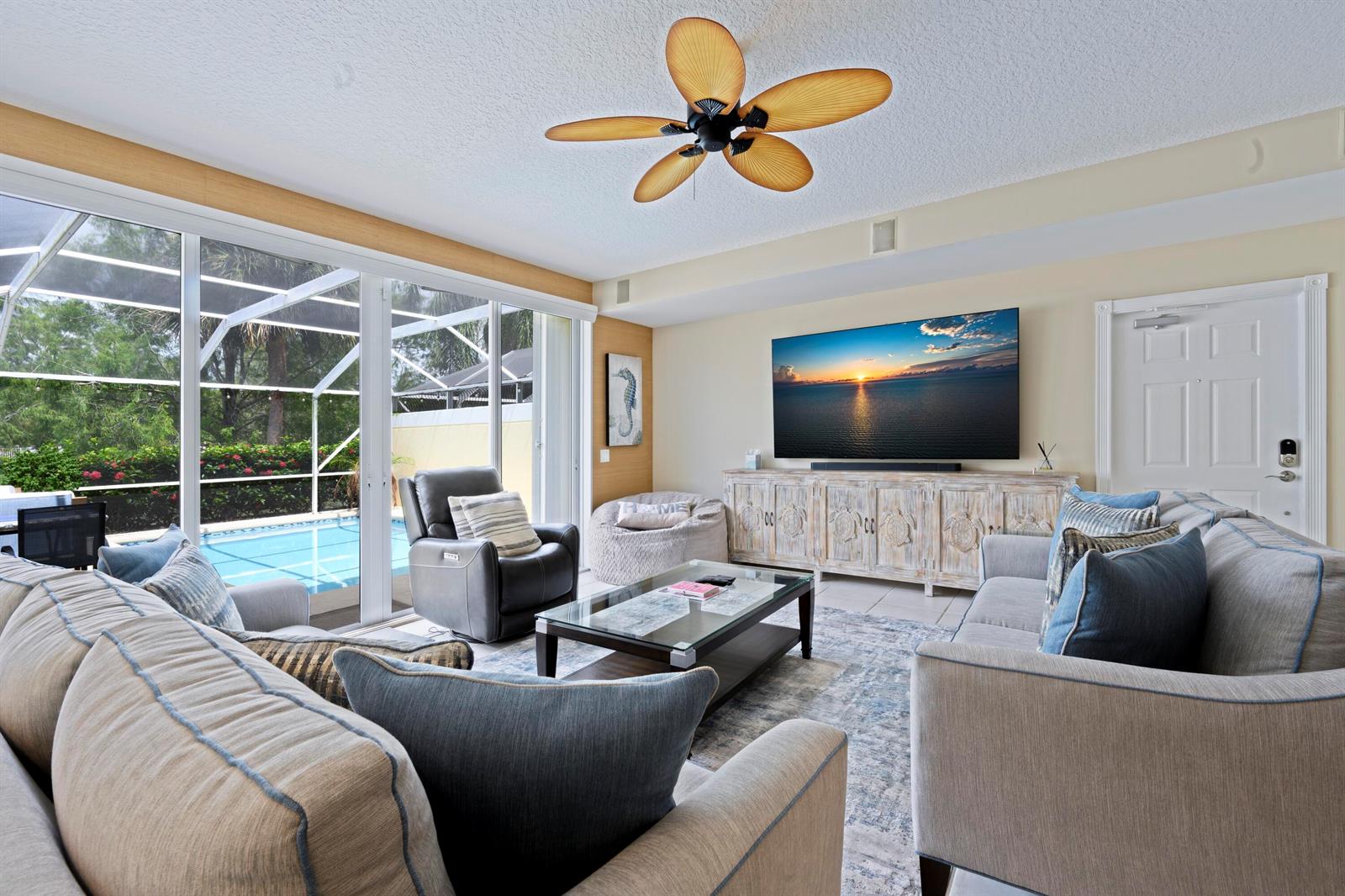 A living room features a large television, a ceiling fan, and sliding doors to a pool — 435 Capistrano Drive, Palm Beach Gardens FL 33410, PALM BEACH GARDENS, FL