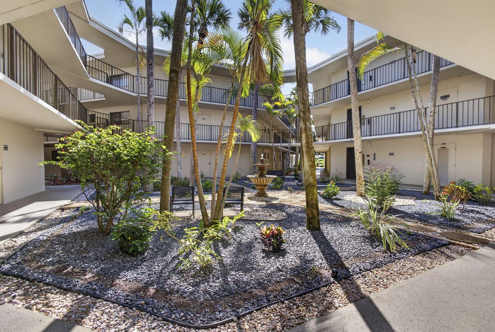 A courtyard with a fountain, palm trees, and gravel landscaping surrounded by a multi-story building — 5340 Las Verdes Circle # 307, Delray Beach FL 33484, DELRAY BEACH, FL