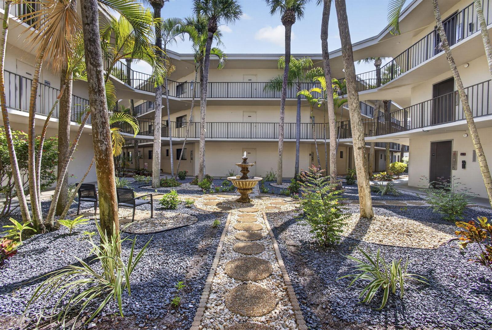 A courtyard with a central fountain, palm trees, and a multi-story apartment building — 5340 Las Verdes Circle # 307, Delray Beach FL 33484, DELRAY BEACH, FL