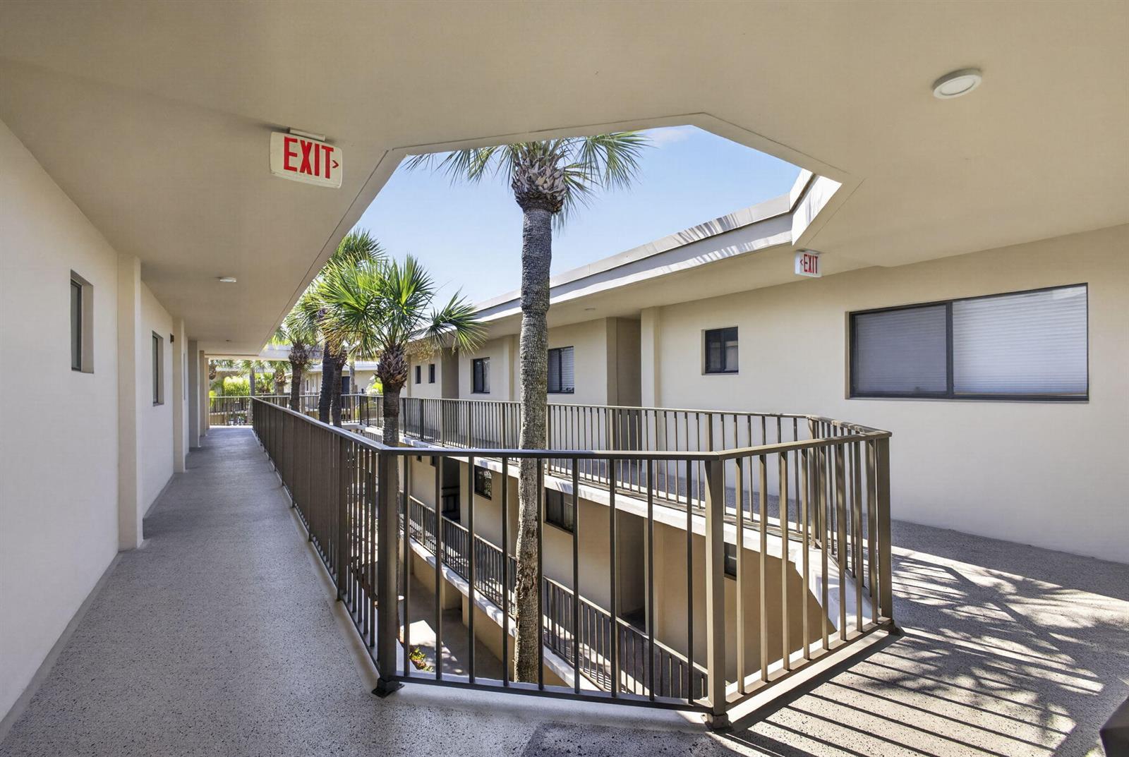 An outdoor apartment building corridor features a central open-air atrium with palm trees — 5340 Las Verdes Circle # 307, Delray Beach FL 33484, DELRAY BEACH, FL