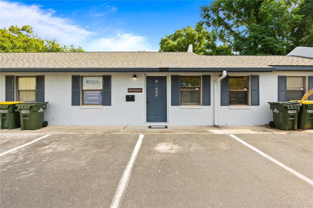 A single-story commercial building exterior with a gray door, windows, and two large trash bins — 684 W MONTROSE STREET UNIT 690/E, CLERMONT, FL
