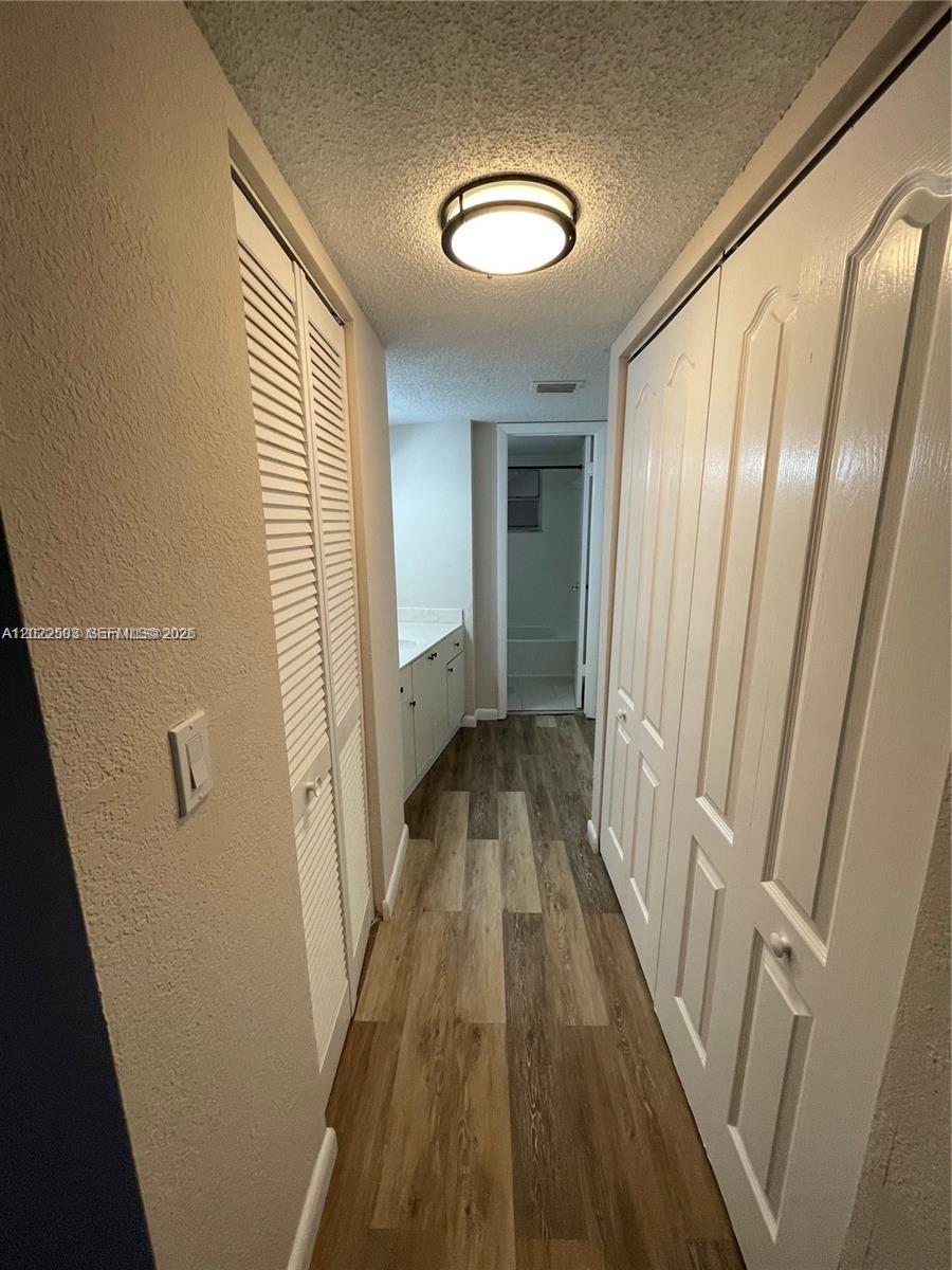 A hallway with wood-look flooring leads to a bathroom vanity and a separate shower area — 4255 N University Dr # 109, Sunrise FL 33351, SUNRISE, FL