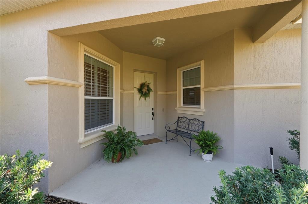 A covered front porch features a white door, a metal bench, and potted ferns — 106 JARDIN LANE, WINTER HAVEN, FL