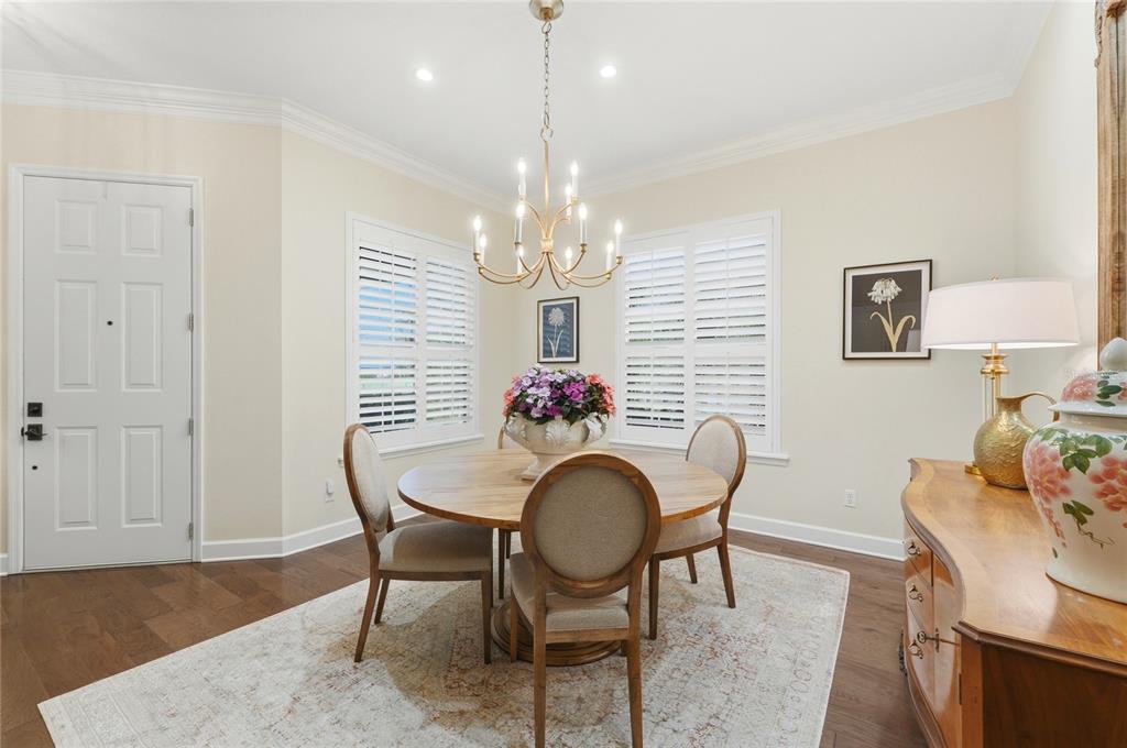 A dining room features a round wooden table, upholstered chairs, a chandelier, and plantation shutters — 106 JARDIN LANE, WINTER HAVEN, FL