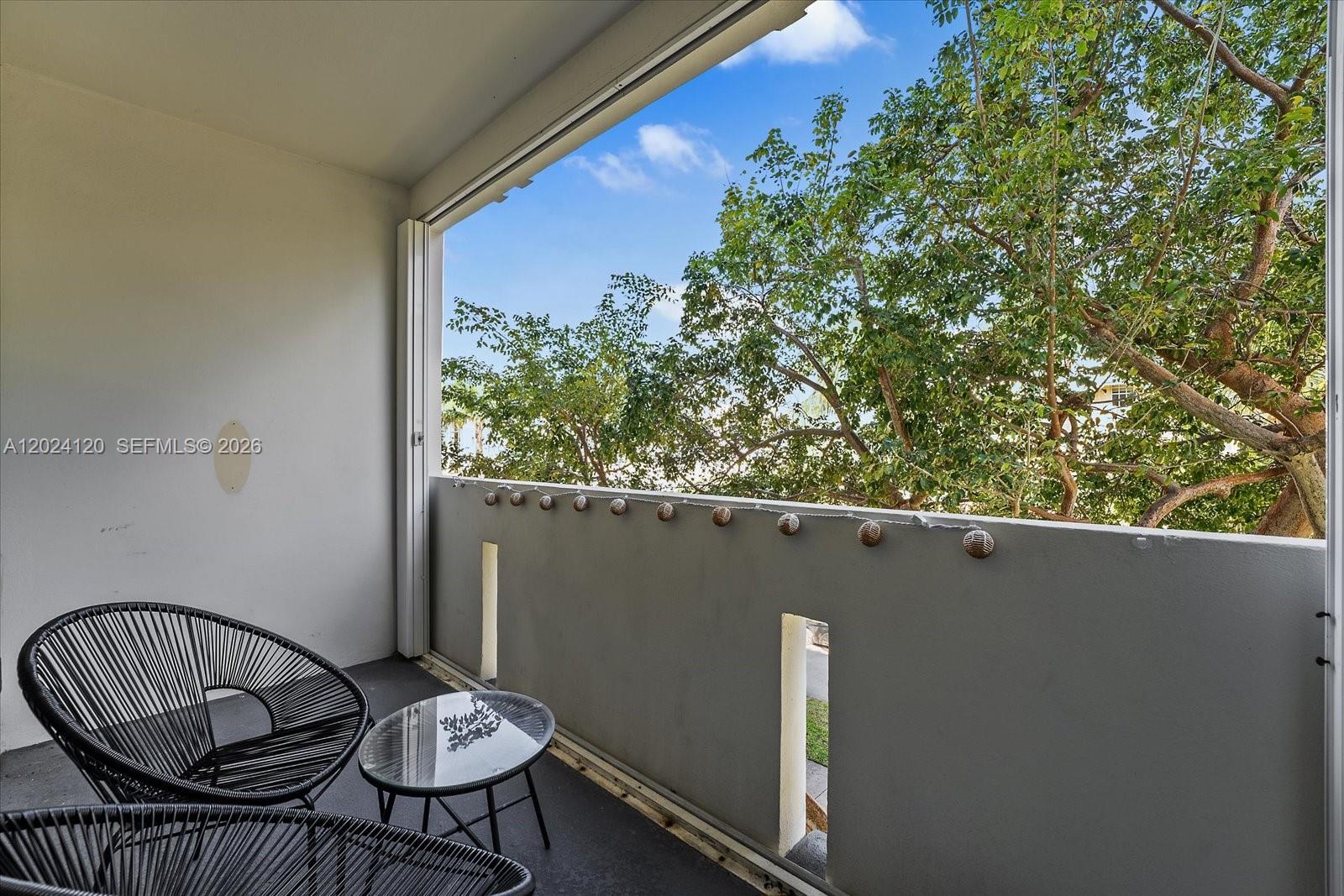 A balcony features two black chairs, a small glass table, and string lights — 300 Galen Dr # 306, Key Biscayne FL 33149, KEY BISCAYNE, FL