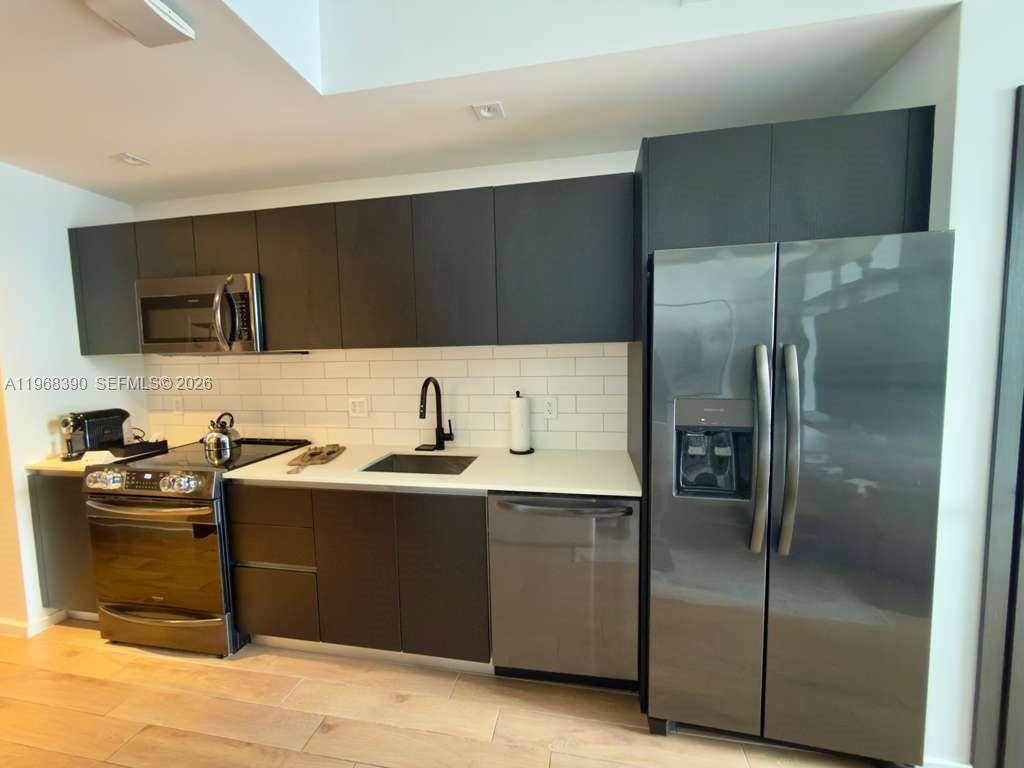 A modern kitchen features dark cabinetry, stainless steel appliances, white countertops, and a subway tile backsplash — 398 NE 5th St # 4313, Miami FL 33132, MIAMI, FL