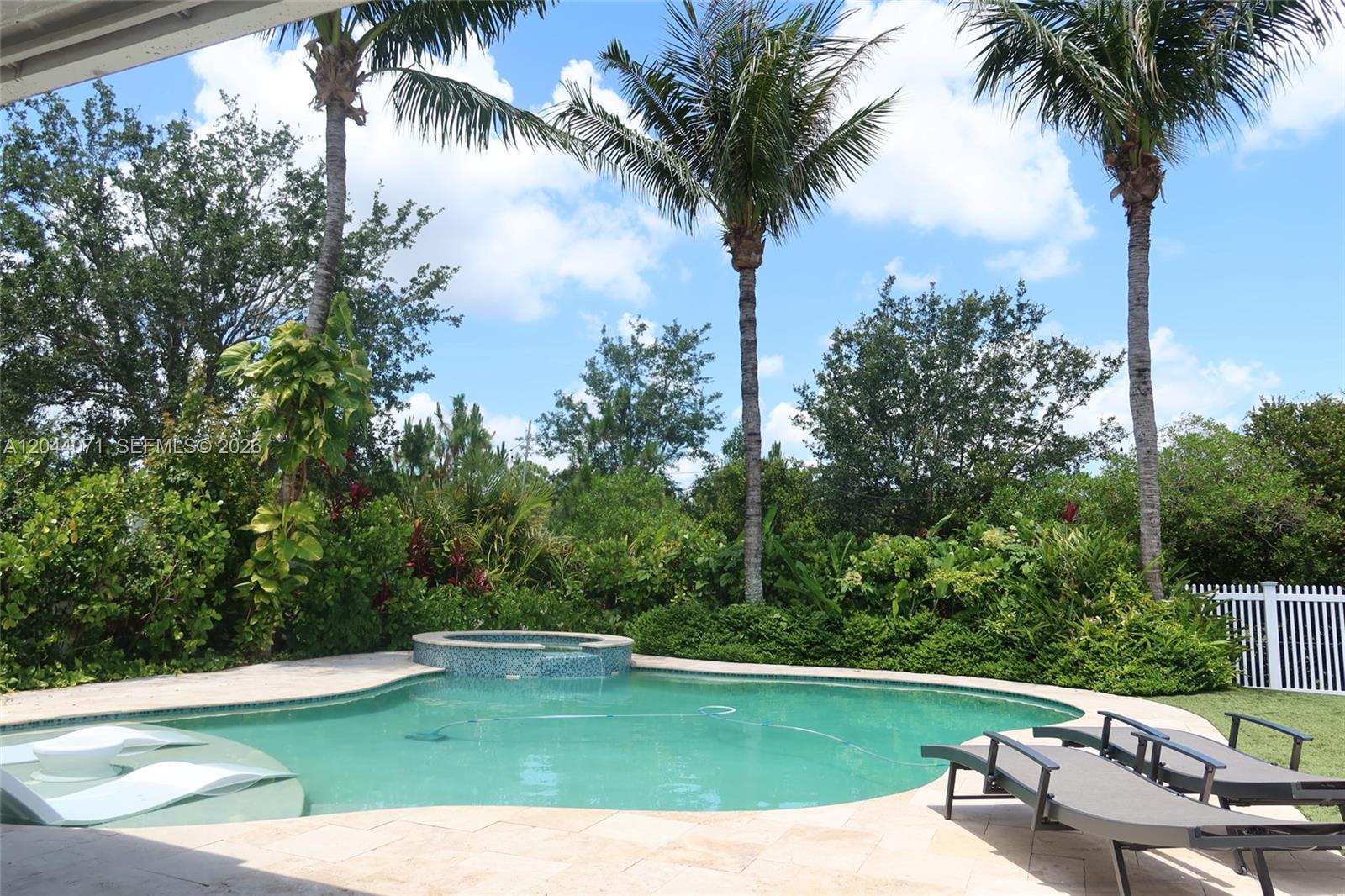 A swimming pool with a spa and lounge chairs sits in a landscaped backyard — 2724 Wymberly Dr, Jupiter FL 33458, JUPITER, FL