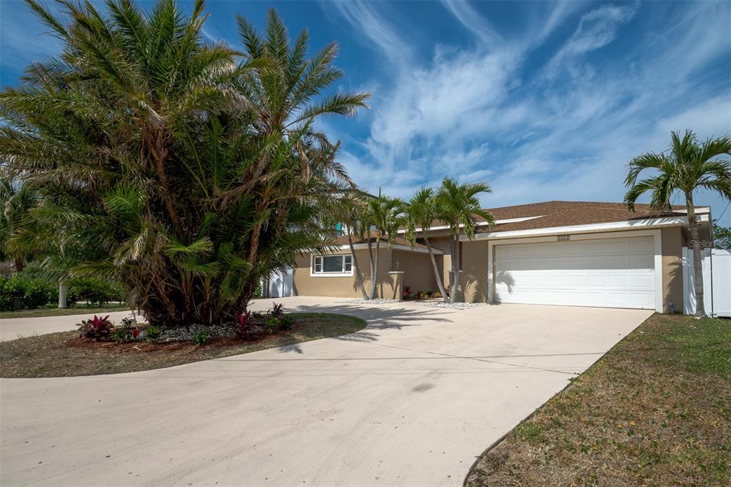A single-story house with a tan exterior, a white garage door, and several palm trees — 2504 HIBISCUS DRIVE W, BELLEAIR BEACH, FL