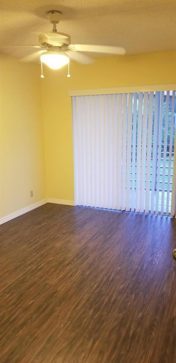 An empty room features wood-look flooring, yellow walls, a ceiling fan, and vertical window blinds — 2000 Springdale Boulevard # 203, Palm Springs FL 33461, PALM SPRINGS, FL