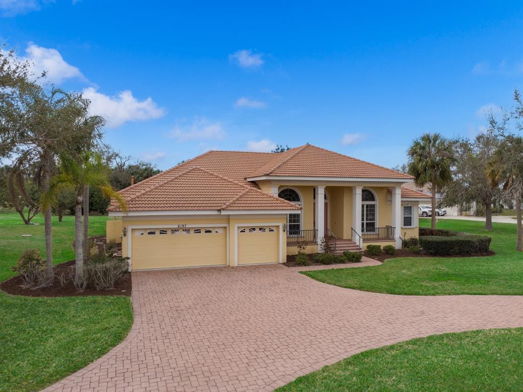 A single-story yellow house with a tile roof and a paved driveway sits on grass — 6197 9TH AVENUE CIRCLE NE, BRADENTON, FL