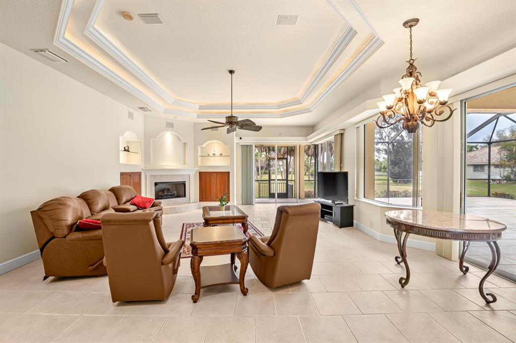 A living room with a tray ceiling, fireplace, tile floors, and a dining area — 6197 9TH AVENUE CIRCLE NE, BRADENTON, FL