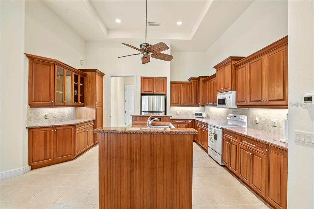 A kitchen features wood cabinets, granite countertops, a center island, and tile flooring — 6197 9TH AVENUE CIRCLE NE, BRADENTON, FL