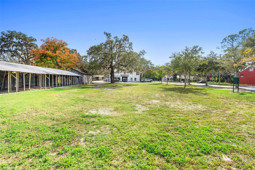 A large, grassy vacant lot features a long, open-sided shed and mature trees — 215 E 5TH STREET, APOPKA, FL