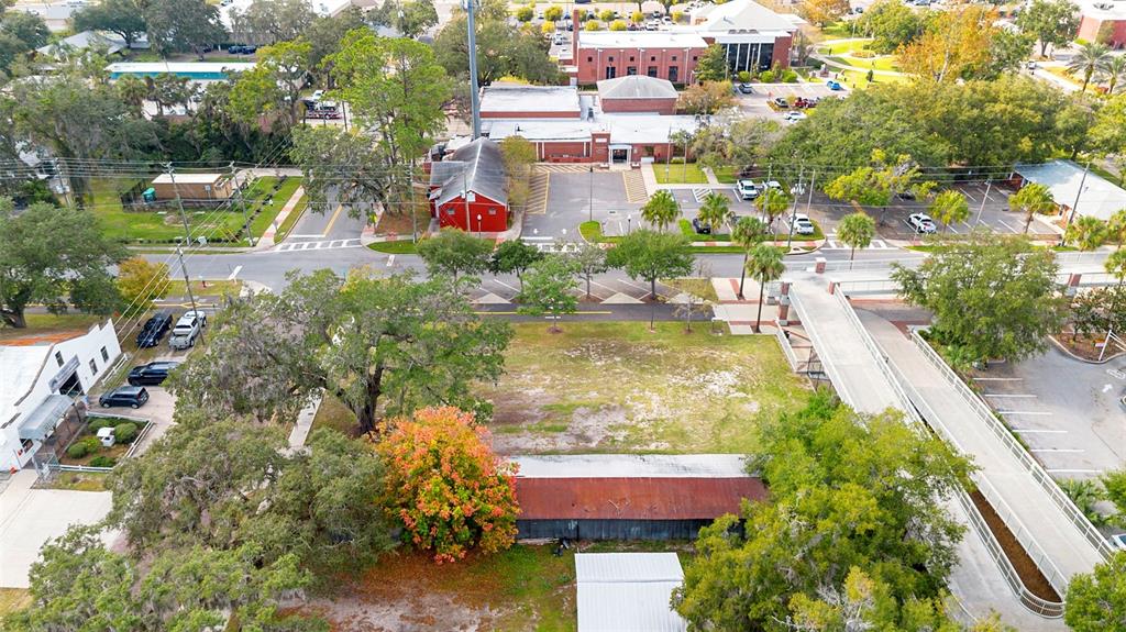An aerial view shows a vacant lot with a rusted shed near a pedestrian bridge — 215 E 5TH STREET, APOPKA, FL