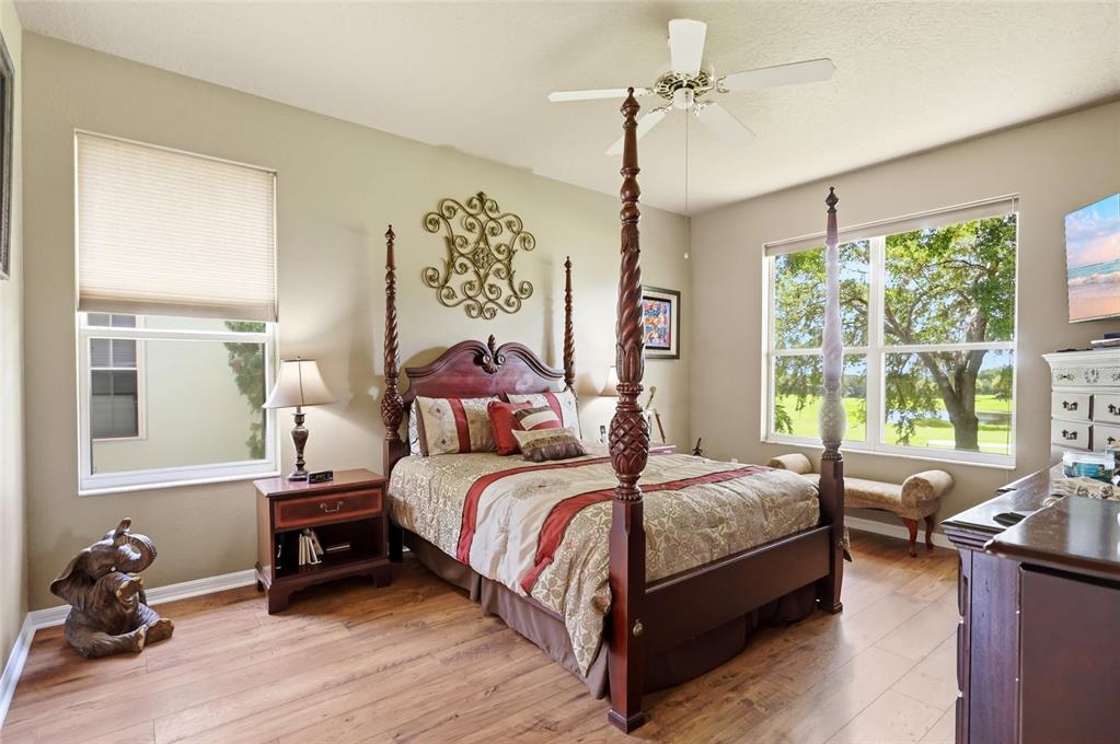 A bedroom features a four-poster wooden bed, wood flooring, and large windows with outdoor views — 3910 LIBERTY HILL DRIVE, CLERMONT, FL