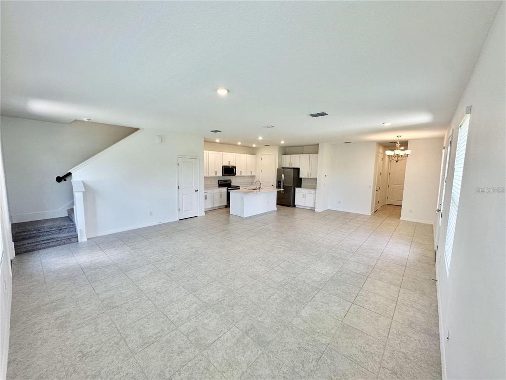 An open-concept living area features light tile flooring, a kitchen with white cabinetry, and stairs — 1707 SANIBEL DRIVE, DAVENPORT, FL