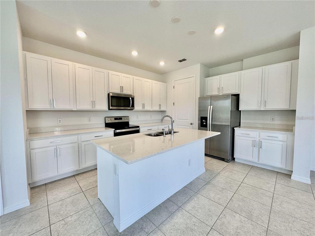A kitchen features white cabinetry, stainless steel appliances, a center island, and light-colored tile flooring — 1707 SANIBEL DRIVE, DAVENPORT, FL