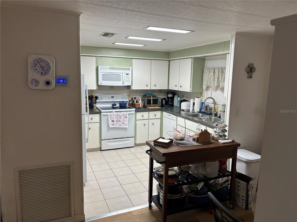 A white mobile home features a metal carport, a screened porch, and a brick planter — 3438 BANBERRY CIRCLE UNIT 1790, ZELLWOOD, FL