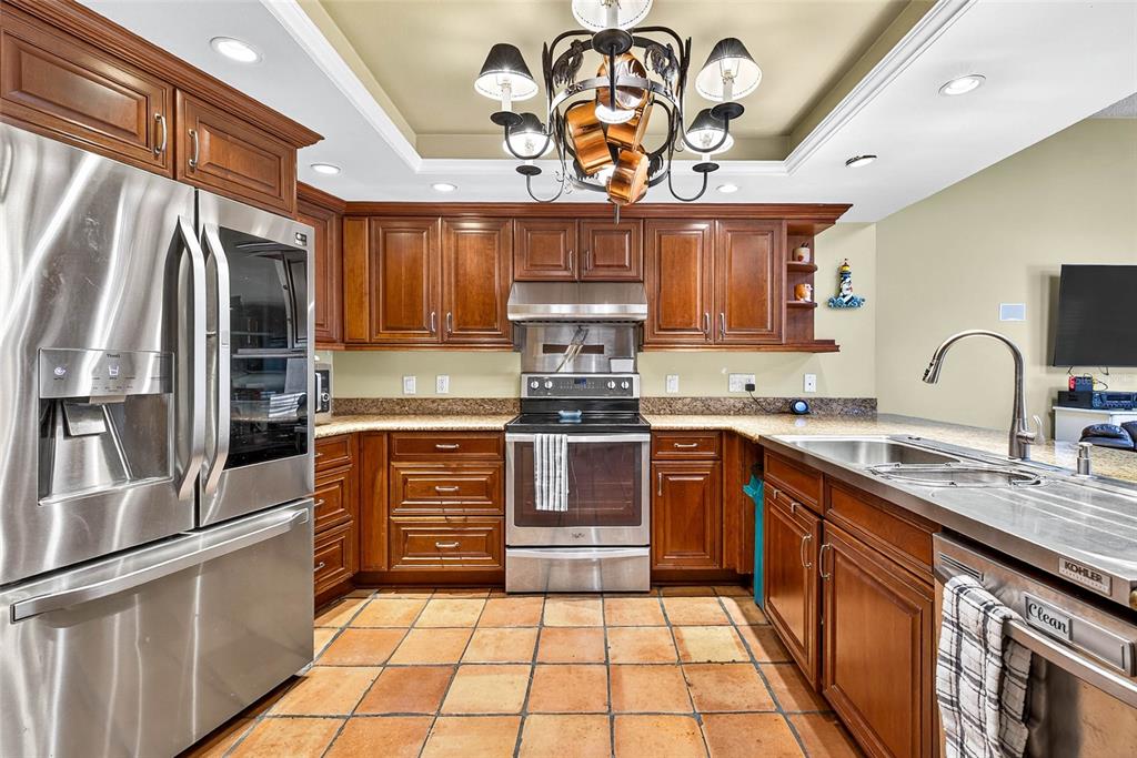 A kitchen features wood cabinets, stainless steel appliances, granite countertops, and terracotta tile flooring — 2835 HAMMOCK DRIVE, PLANT CITY, FL