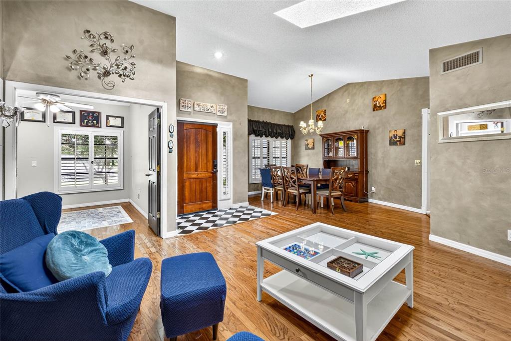 A living room with hardwood floors, a blue armchair, and a dining area beyond — 2835 HAMMOCK DRIVE, PLANT CITY, FL