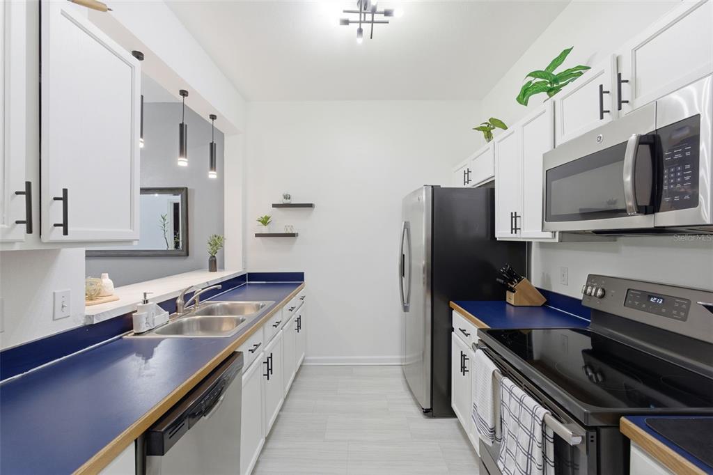 A galley kitchen features white cabinets, blue countertops, stainless steel appliances, and light tile flooring — 1224 S HIAWASSEE ROAD UNIT 630, ORLANDO, FL