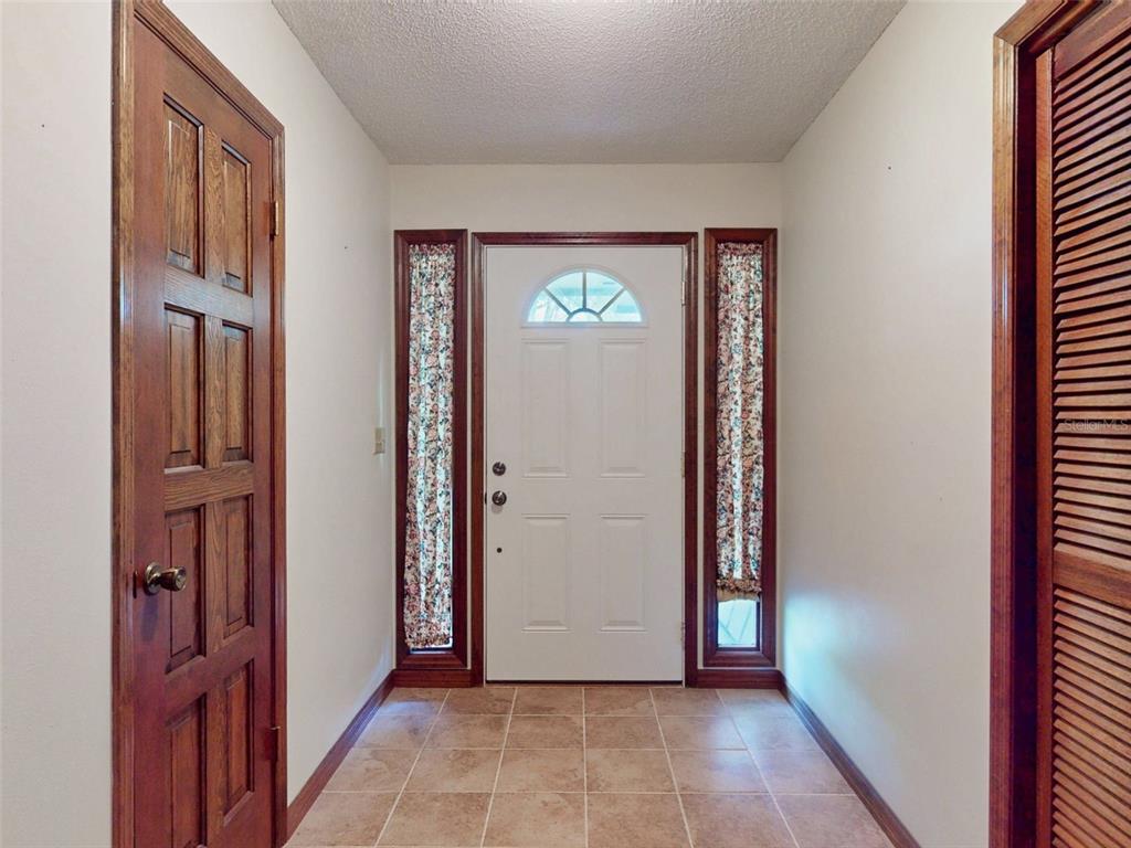 A tiled entryway features a white front door with sidelights and wood-trimmed doors — 799 E LEHIGH DRIVE, DELTONA, FL