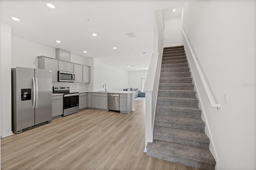 A kitchen with stainless steel appliances and light wood flooring next to a carpeted staircase — 5055 SUNRISE ESTATES DRIVE, MELBOURNE, FL