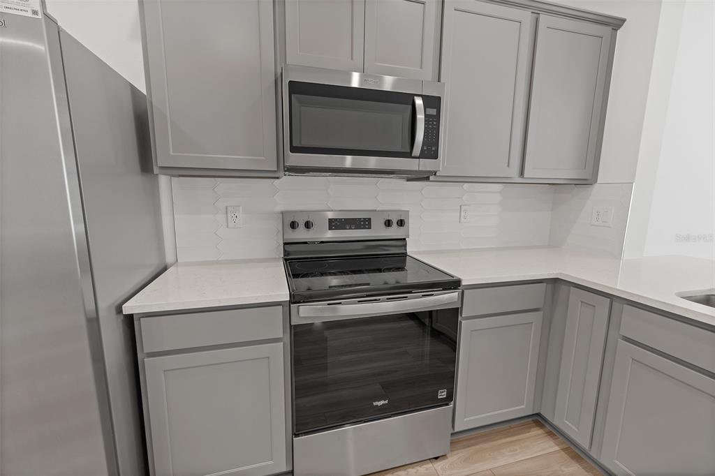 A kitchen features gray cabinets, stainless steel appliances, white countertops, and a white tile backsplash — 5055 SUNRISE ESTATES DRIVE, MELBOURNE, FL