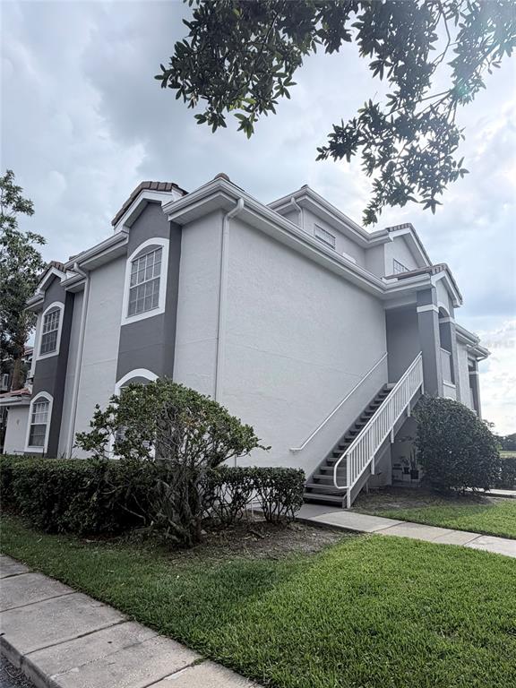 A two-story apartment building exterior features light gray stucco walls, dark gray accents, and stairs — 13827 FAIRWAY ISLAND DRIVE UNIT 1228, ORLANDO, FL