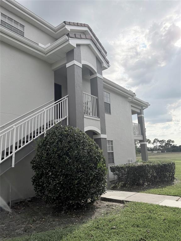 A two-story apartment building exterior features a white staircase, grey accents, and landscaped bushes — 13827 FAIRWAY ISLAND DRIVE UNIT 1228, ORLANDO, FL