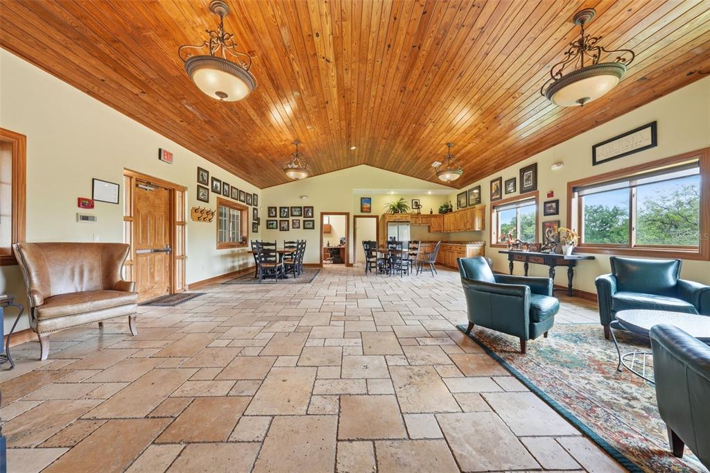 A spacious room with a vaulted wood ceiling, stone tile flooring, and multiple seating areas — 2020 HAAS ROAD, APOPKA, FL