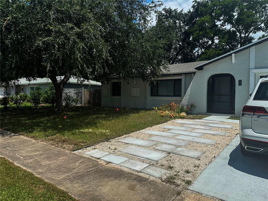 A single-story house with a light-colored exterior, a gravel driveway, and a large shade tree — 1721 FREEMAN DRIVE, KISSIMMEE, FL
