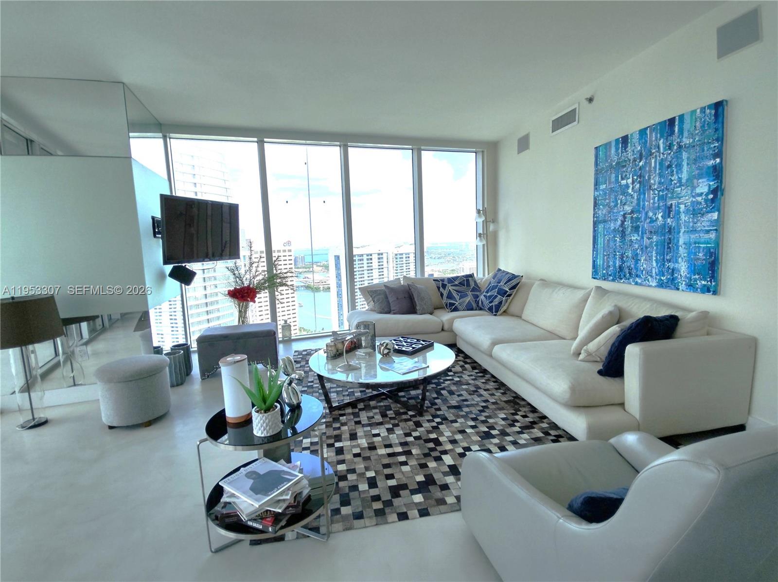A modern living room features a white sectional sofa, a patterned rug, and floor-to-ceiling windows — 465 Brickell Ave # 4402, Miami FL 33131, MIAMI, FL