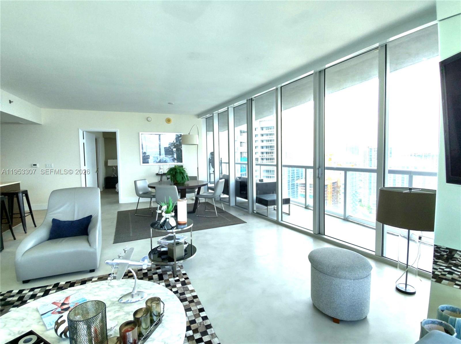 A modern living and dining area features floor-to-ceiling windows overlooking a city skyline — 465 Brickell Ave # 4402, Miami FL 33131, MIAMI, FL