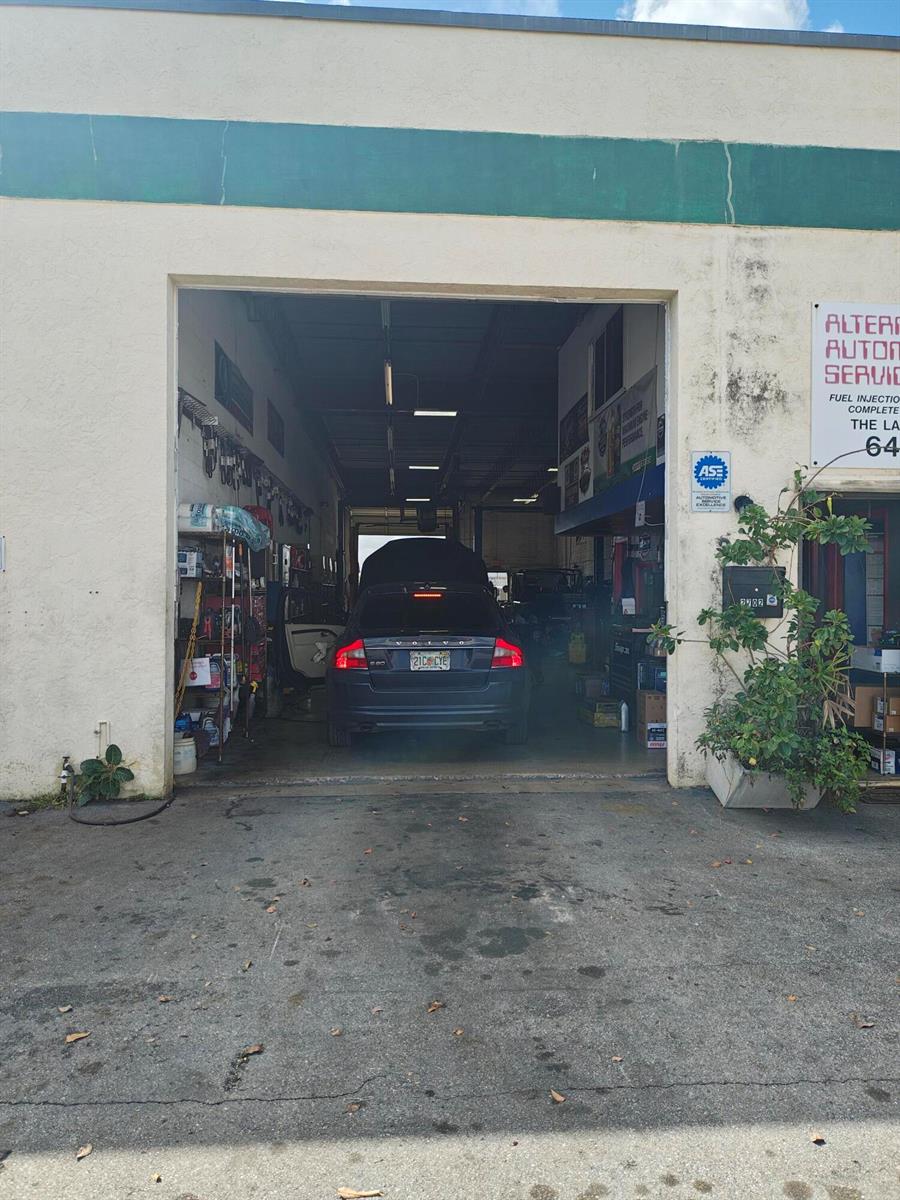 A dark Volvo is parked inside an open automotive repair garage bay — 2702 Rockey Drive, West Palm Beach FL 33409, WEST PALM BEACH, FL