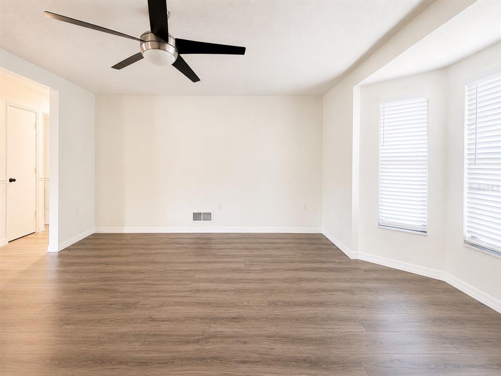 An empty room features wood-look flooring, white walls, a ceiling fan, and a bay window — 3209 PAFKO DRIVE, SARASOTA, FL