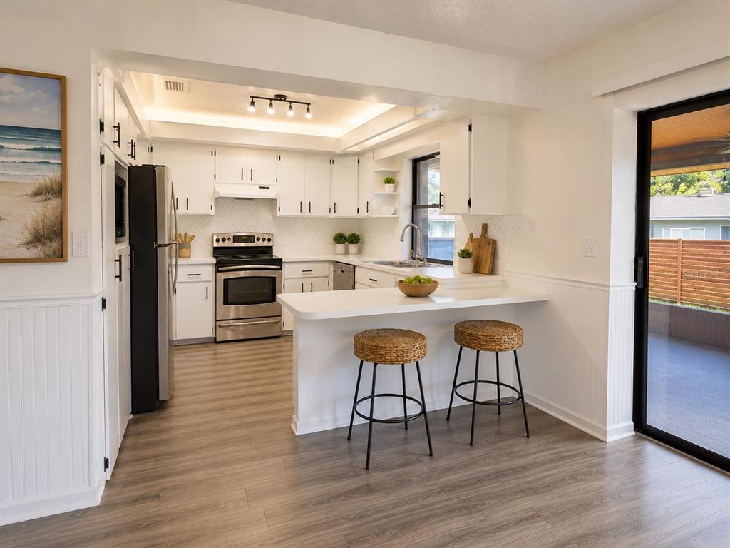A white kitchen features a breakfast bar, stainless steel appliances, and wood-look flooring — 3209 PAFKO DRIVE, SARASOTA, FL