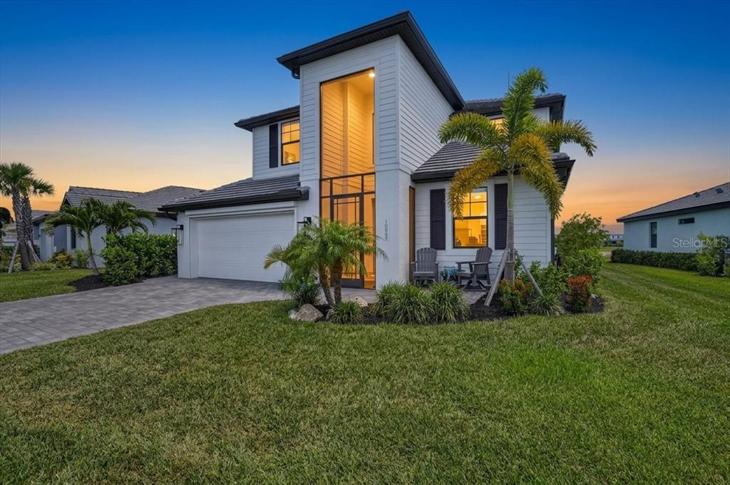 A two-story white house with a tall glass entryway and a two-car garage at dusk — 10865 SUN DROP STREET, VENICE, FL
