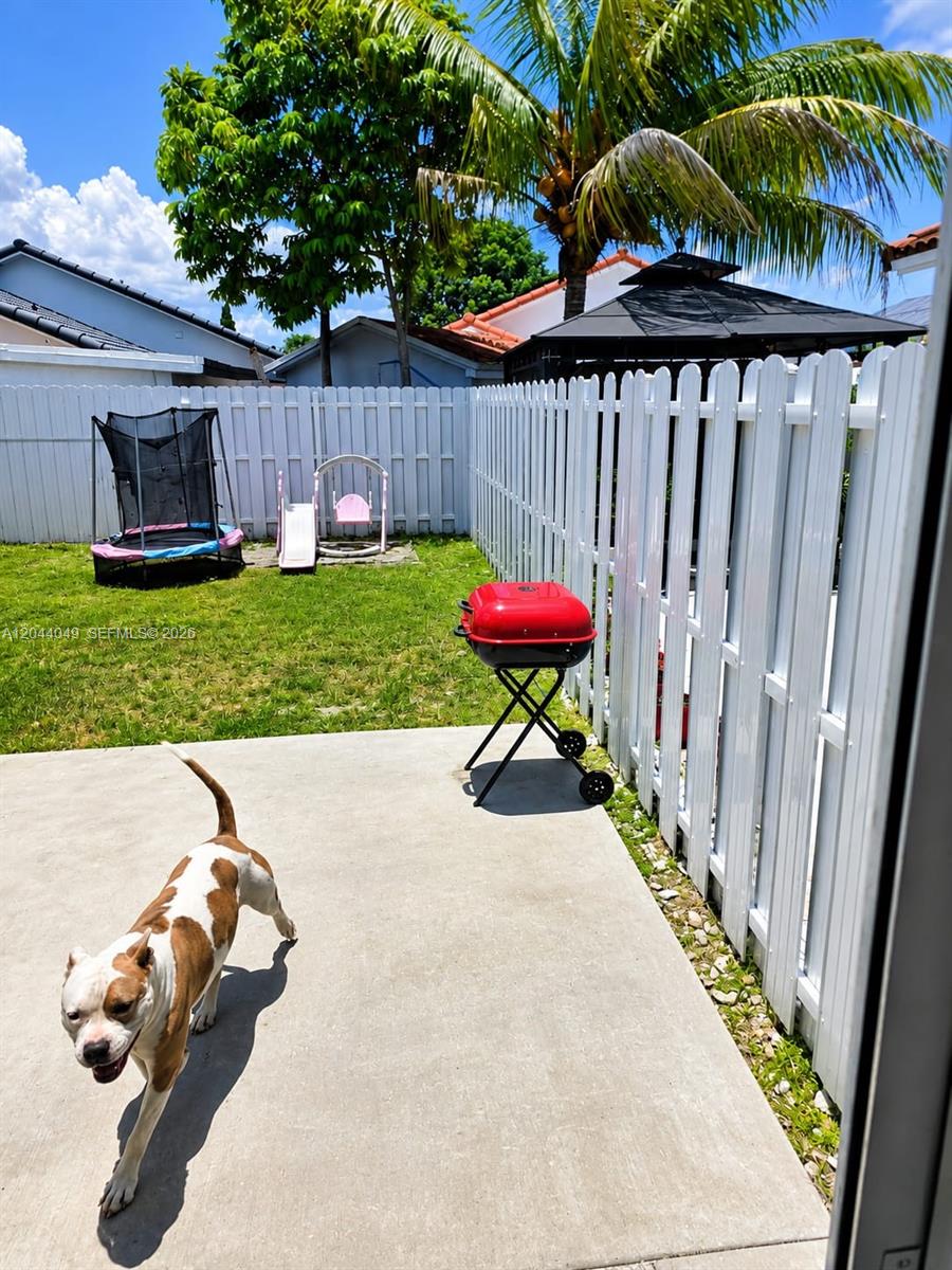 A backyard features a concrete patio, a red charcoal grill, a trampoline, and a dog — 17834 SW 144th Ct # 0, Miami FL 33177, MIAMI, FL