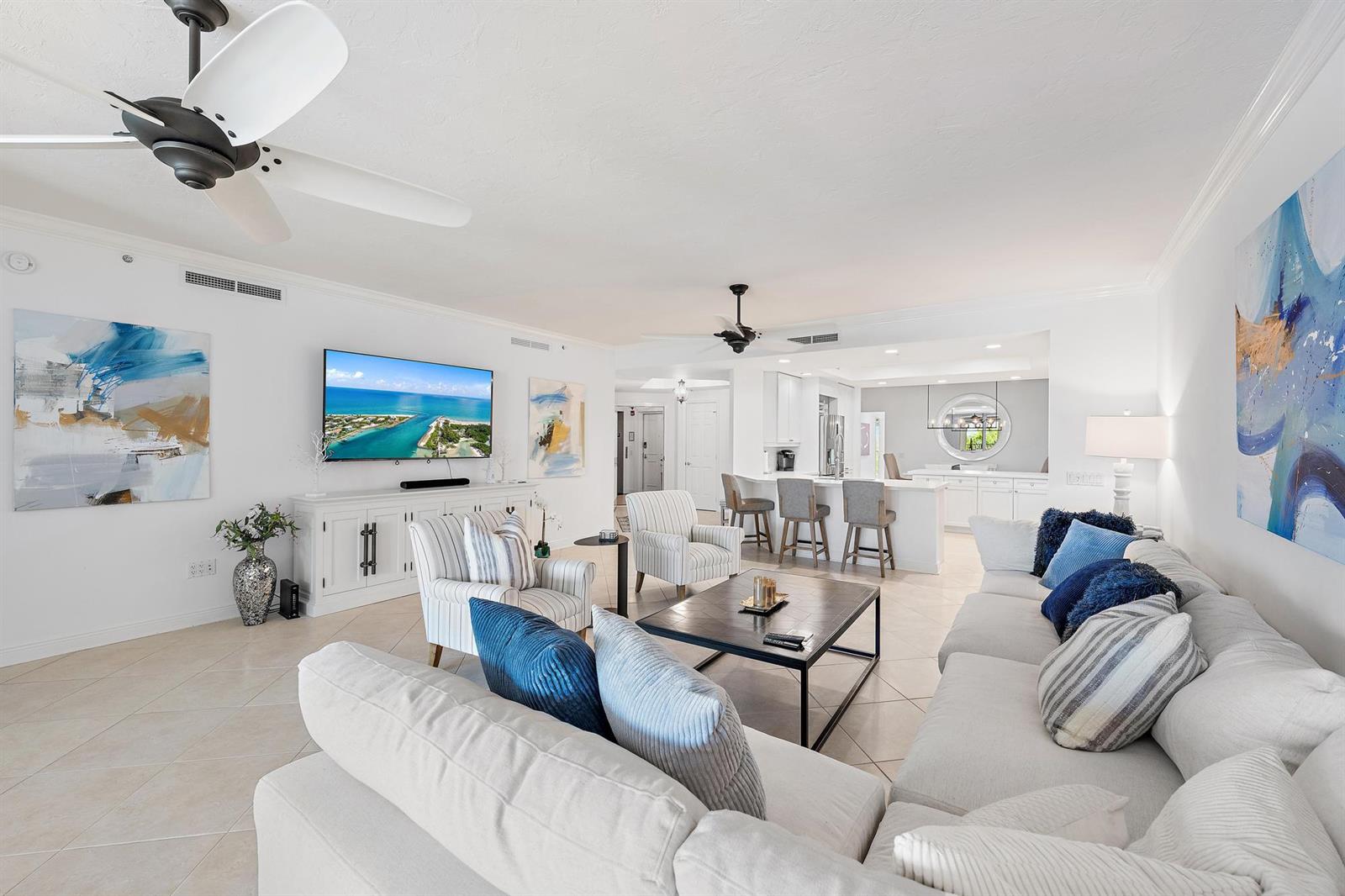 A bright, open-concept living room features white furniture, blue accent pillows, and a large television — 400 S Us Hwy 1 # 303, Jupiter FL 33477, JUPITER, FL