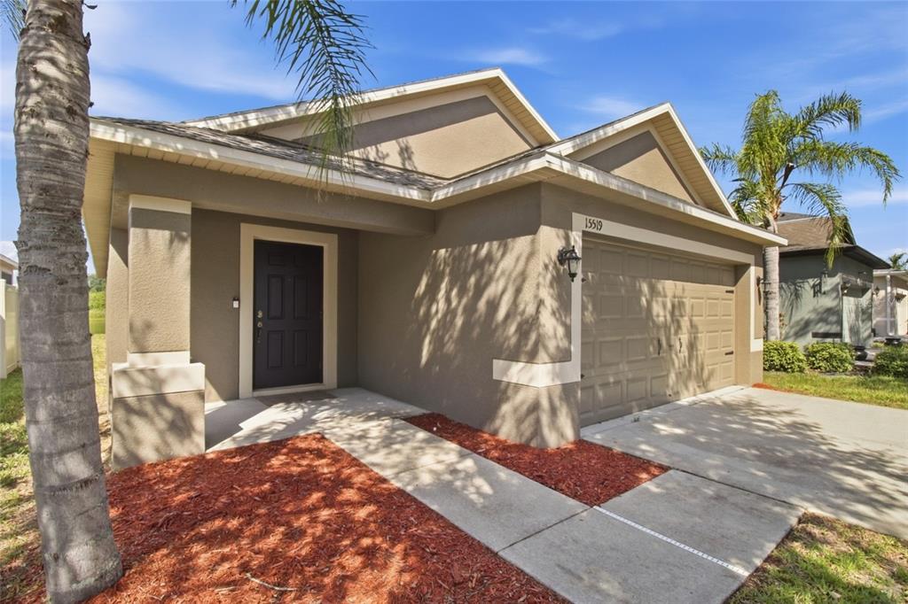 A single-story house with a tan stucco exterior, a dark front door, and a garage — 15519 TELFORD SPRING DRIVE, SUN CITY CENTER, FL