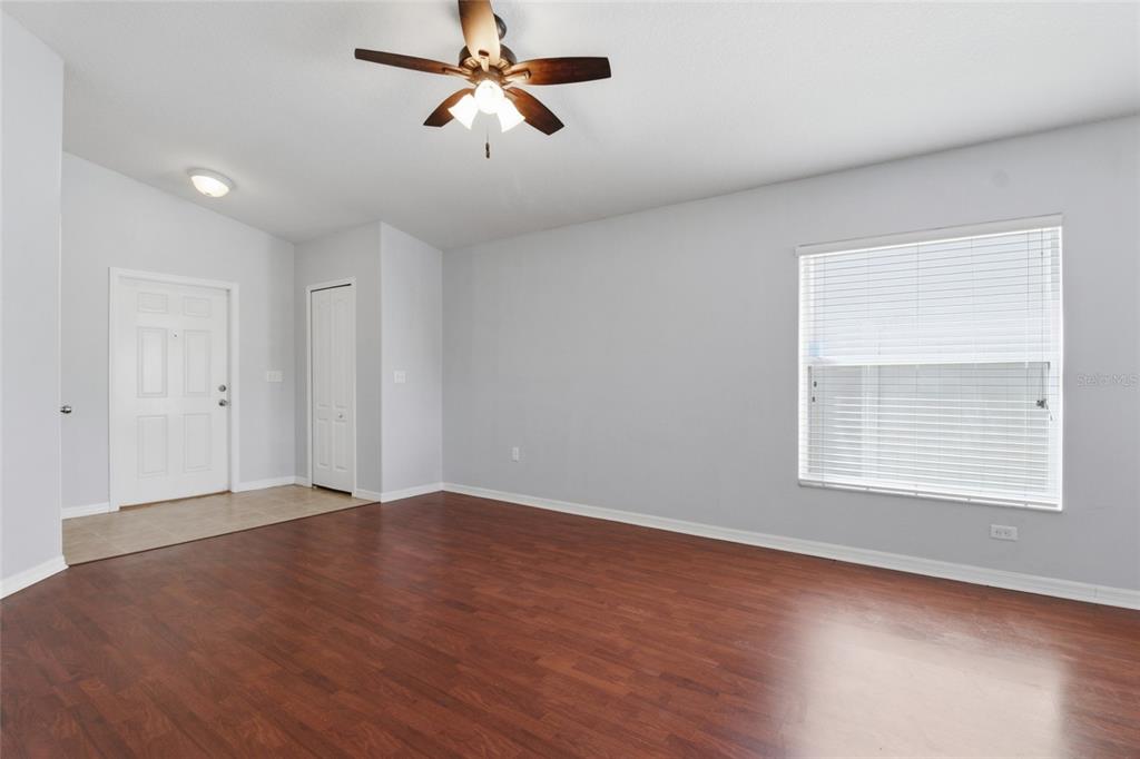 A living room with light gray walls, wood-look flooring, a ceiling fan, and a window — 15519 TELFORD SPRING DRIVE, SUN CITY CENTER, FL