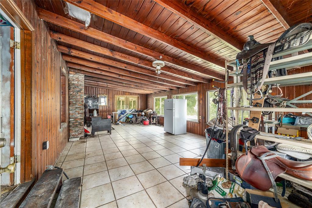 A rustic room with wood-paneled walls, exposed ceiling beams, tile flooring, and equestrian equipment — 11768 N GATLEN AVENUE, DUNNELLON, FL
