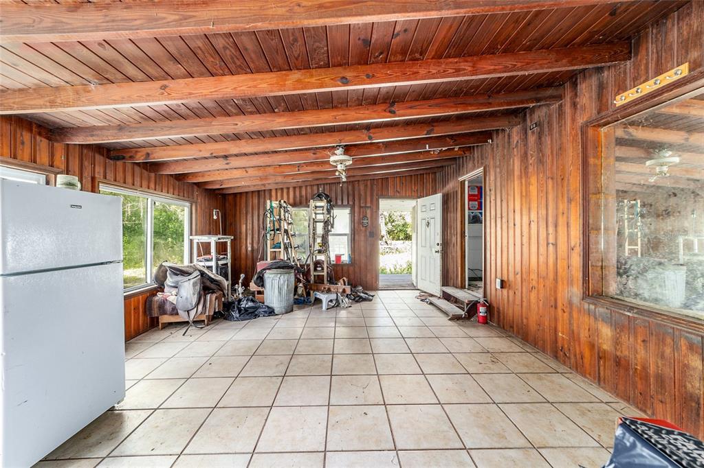 A rustic room with wood-paneled walls, exposed ceiling beams, and light-colored tile flooring — 11768 N GATLEN AVENUE, DUNNELLON, FL