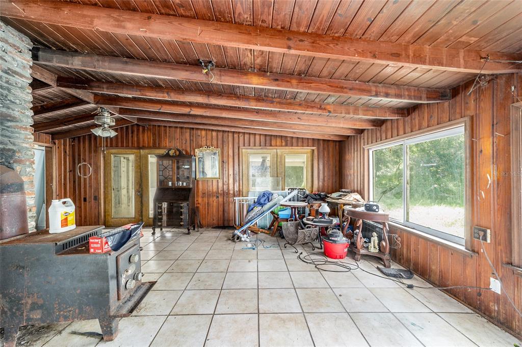 A sunroom with wood-paneled walls, a beamed ceiling, tile flooring, and a wood-burning stove — 11768 N GATLEN AVENUE, DUNNELLON, FL