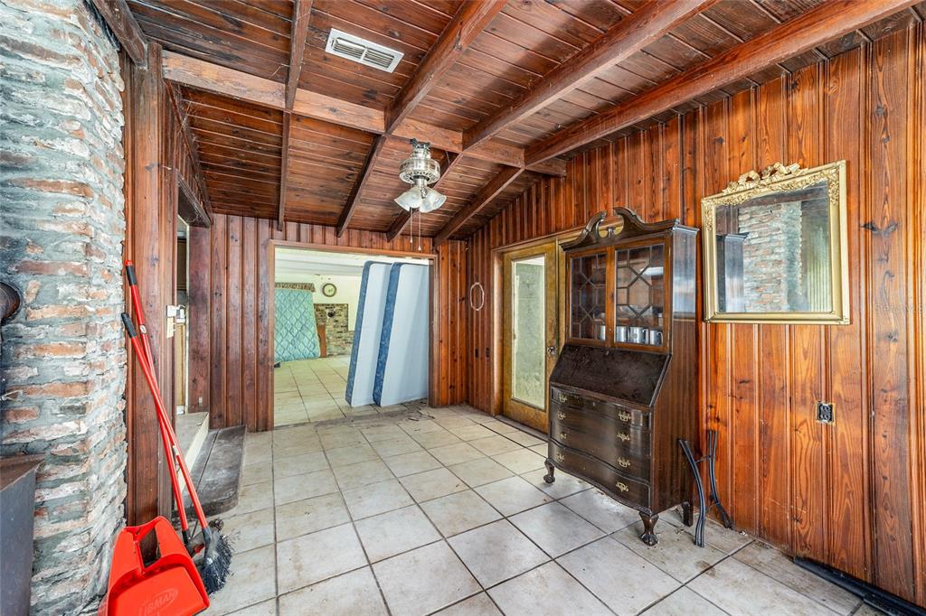 A room with wood-paneled walls, a beamed ceiling, tile flooring, and a vintage secretary desk — 11768 N GATLEN AVENUE, DUNNELLON, FL